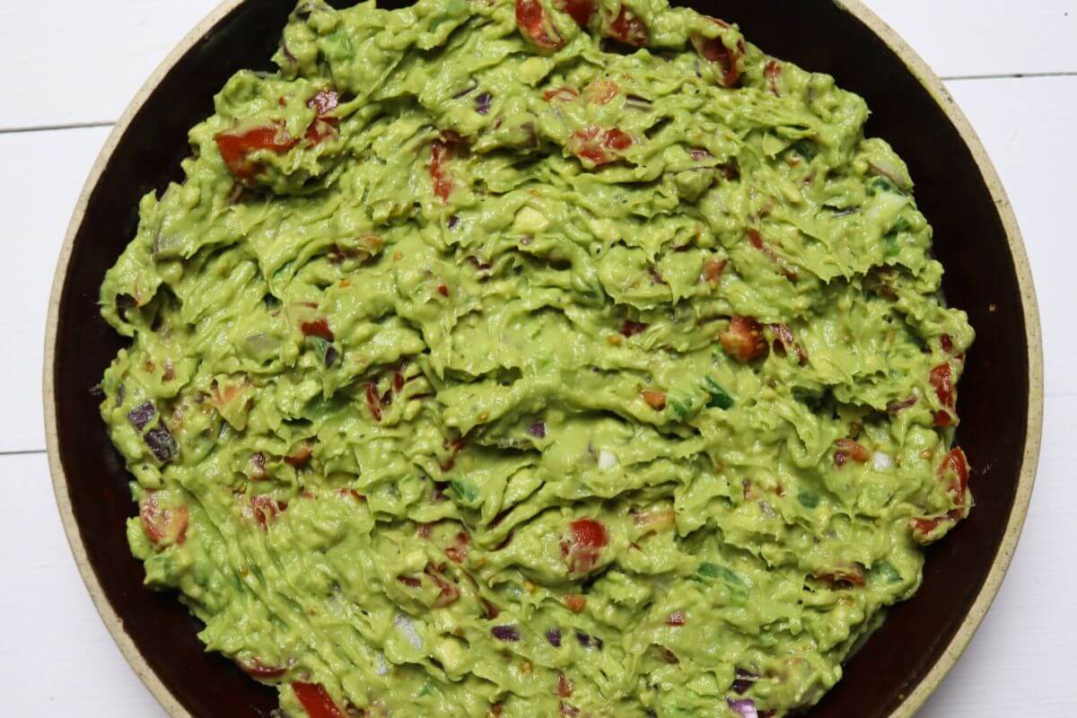 Bowl of guacamole with diced tomatoes and red onion mixed throughout.