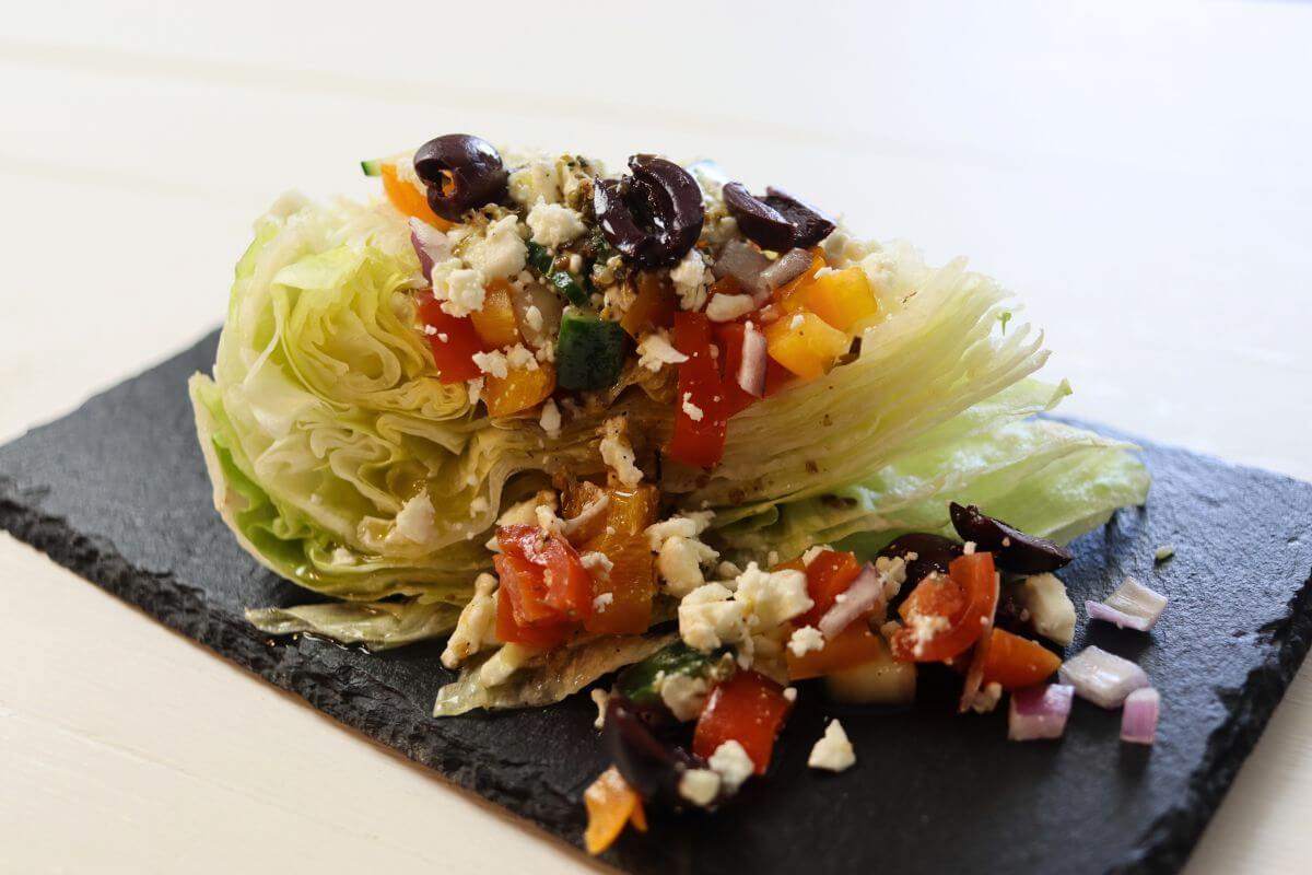 Greek wedge salad with diced vegetables, feta, and olives on a slate board.