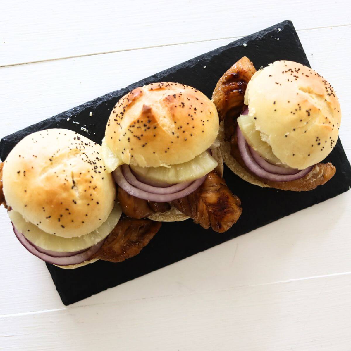 Grilled teriyaki chicken sliders with pineapple and red onion on poppy seed rolls.