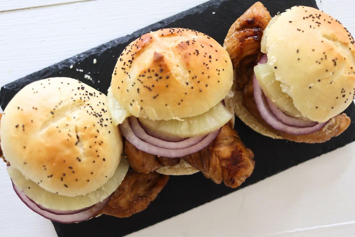 Three chicken sliders with pineapple rings and red onion slices on seeded buns.