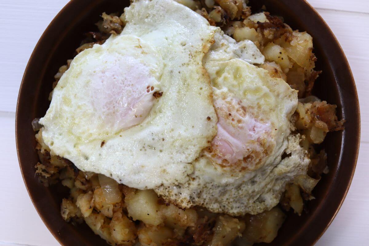 Two fried eggs resting over diced potatoes and onions in a bowl.