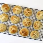 Freshly baked mini rolls with scored tops arranged on black cooling rack.