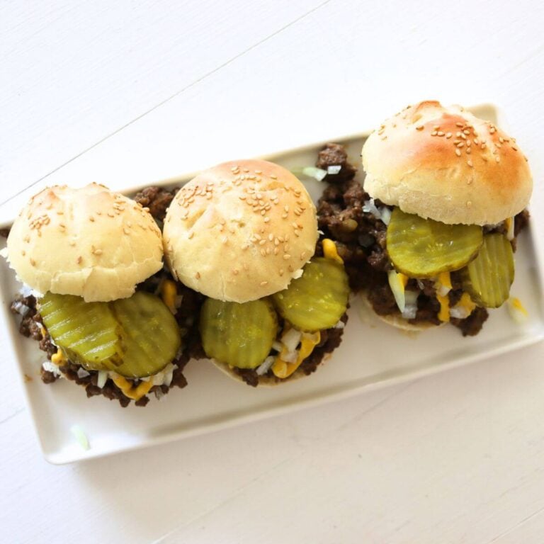 Loose meat sliders with pickles, diced onion, and mustard on a white plate.