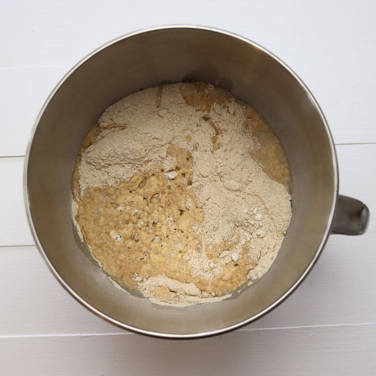Flour and yeast mixture combined with water in stand mixer bowl before kneading.