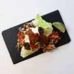 Iceberg wedge topped with ground beef, shredded cheese, tomatoes, olives, sour cream, and salsa on black board.