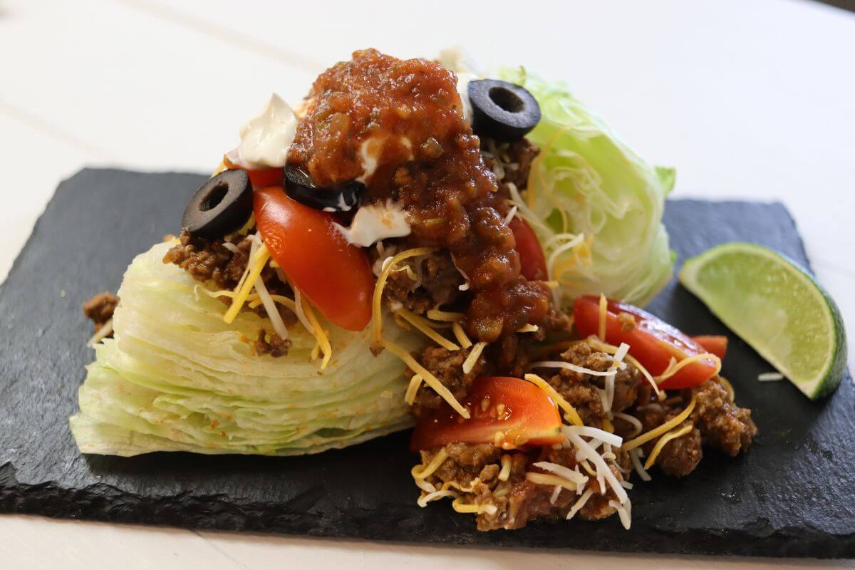 Taco wedge salad with ground beef, cheese, tomatoes, olives, and salsa on iceberg wedge.