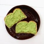 Two slices of avocado toast on a dark brown ceramic plate.