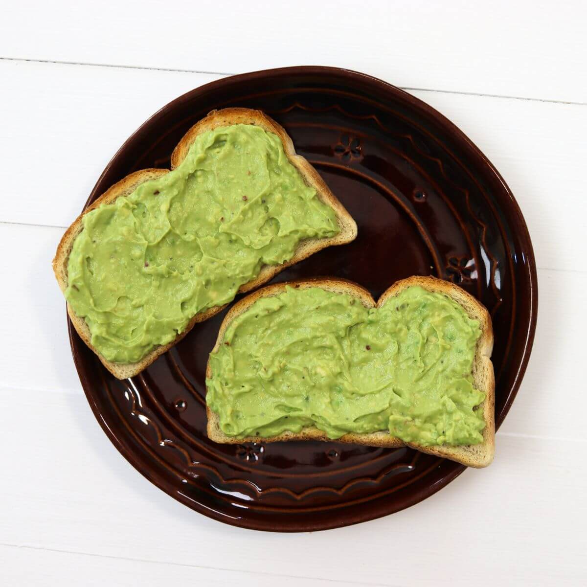 Two slices of avocado toast on a dark brown ceramic plate.