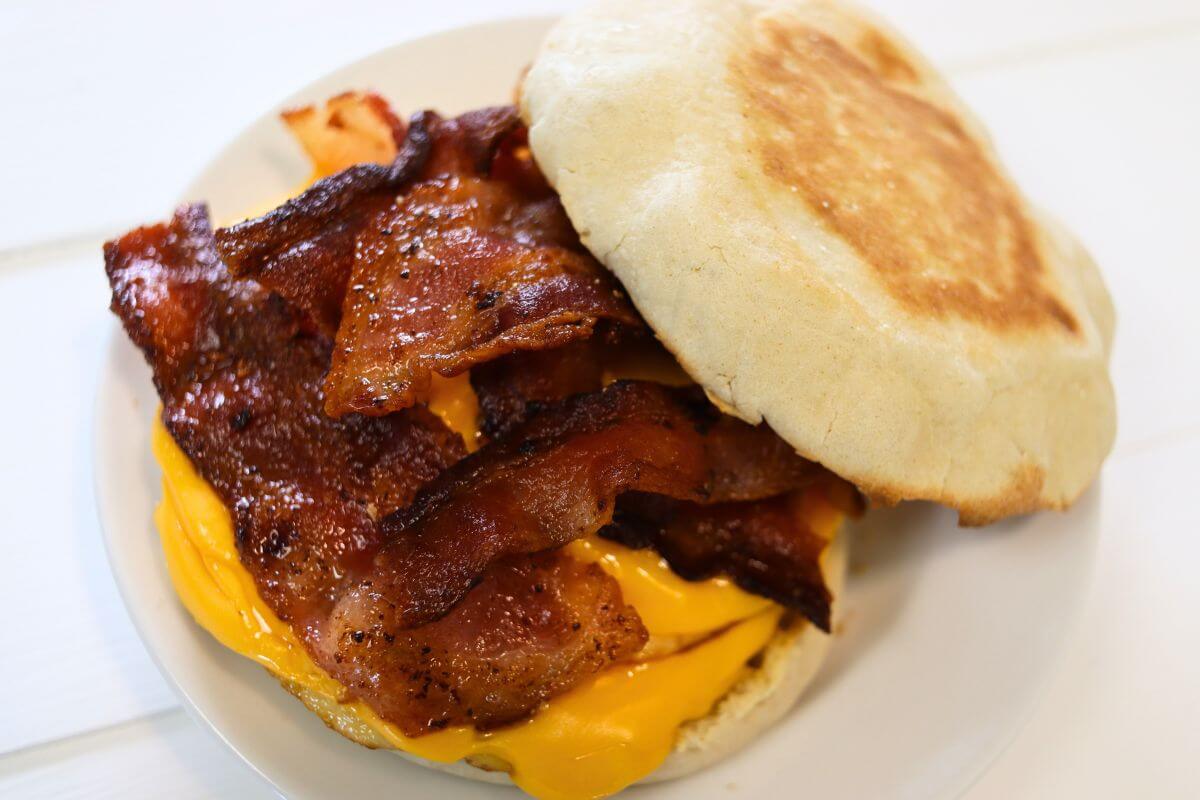 Bacon and egg muffin sandwich with melted cheese and stacked bacon on a plate.