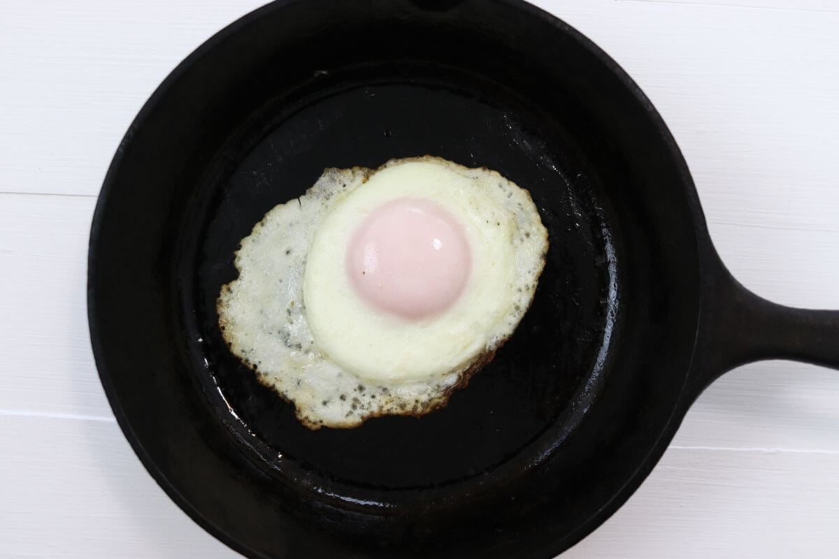 Basted egg in a cast iron skillet on a white surface.