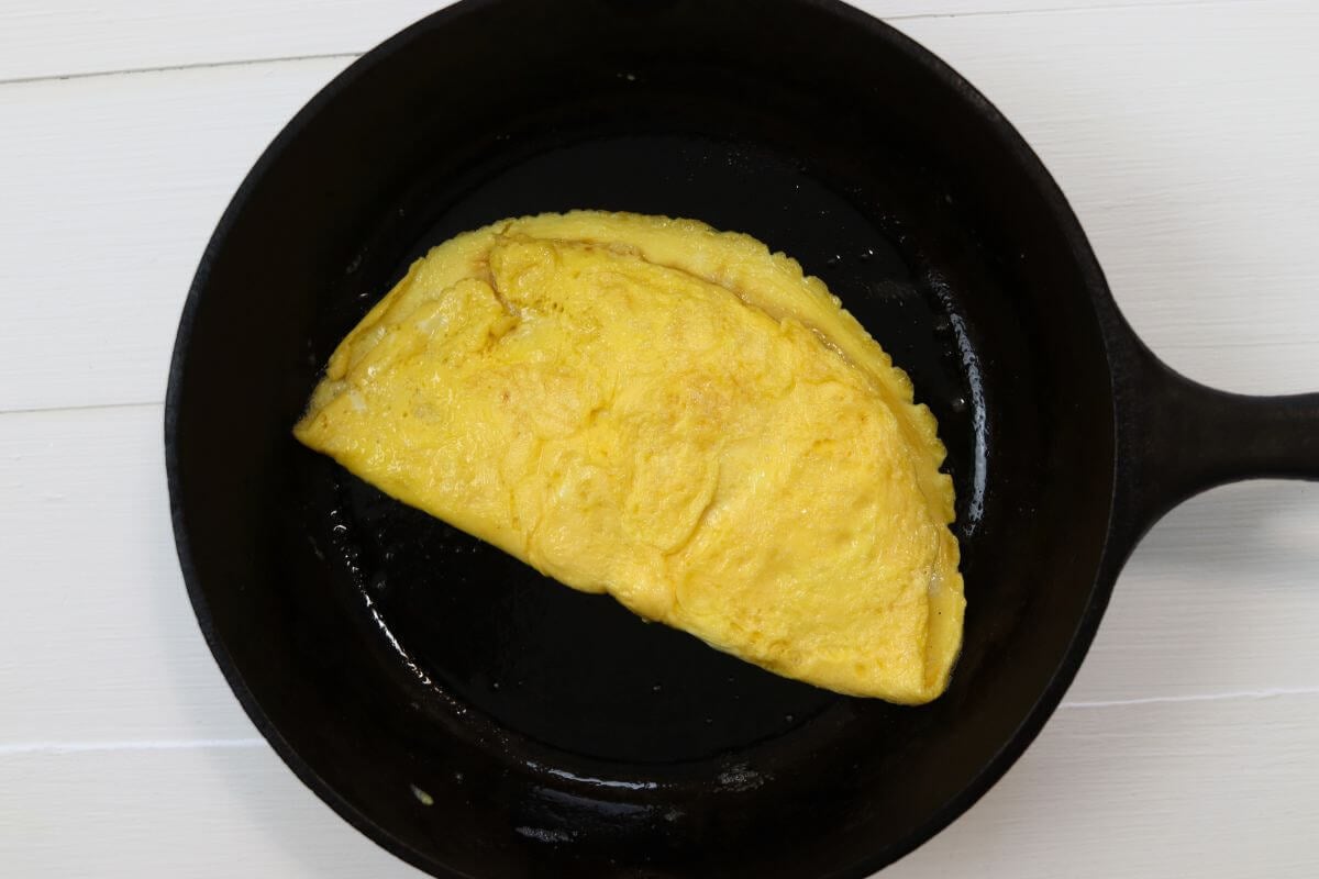 Omelet style egg in a cast iron skillet on a white surface.
