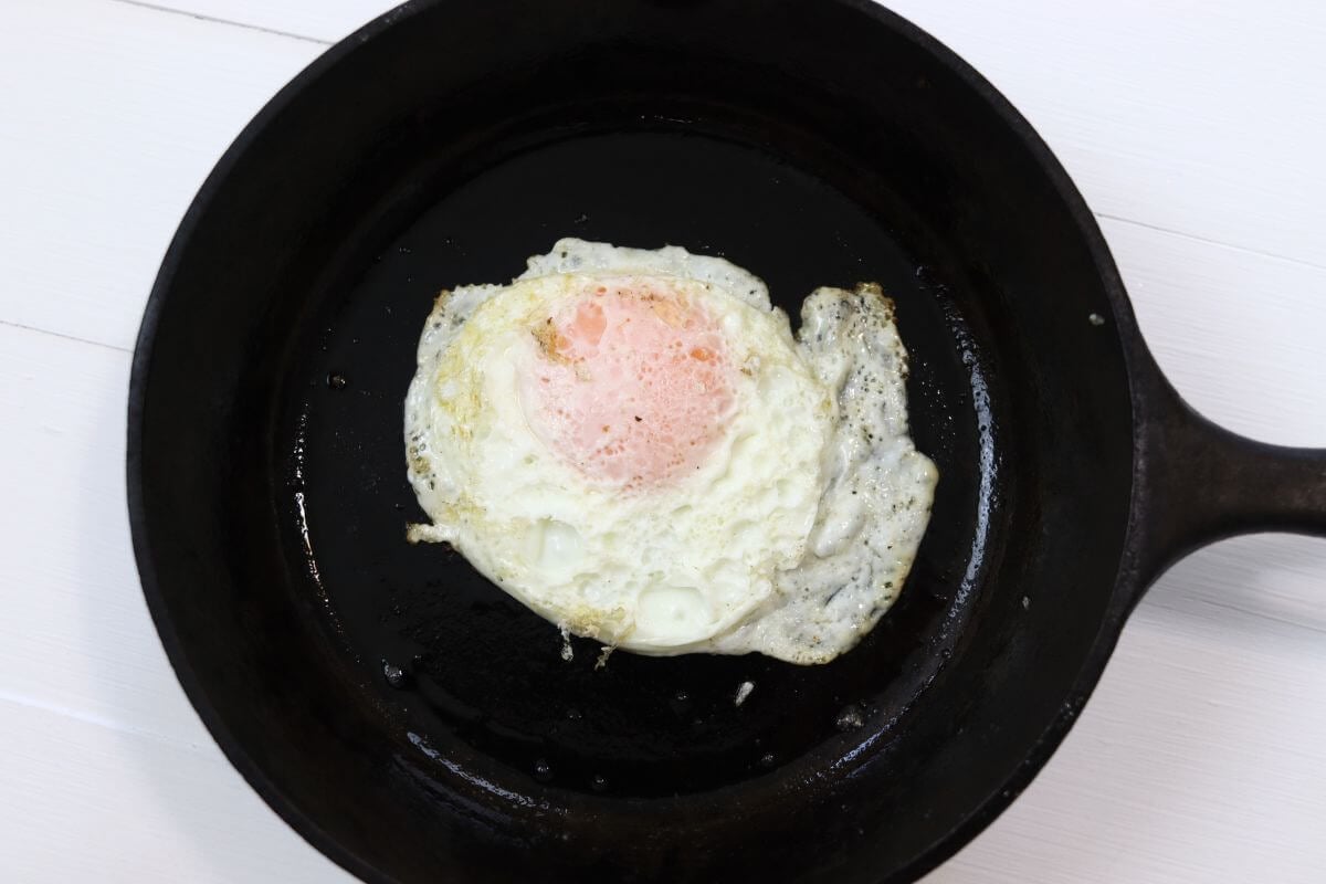 Over easy egg in a cast iron skillet on a white surface.