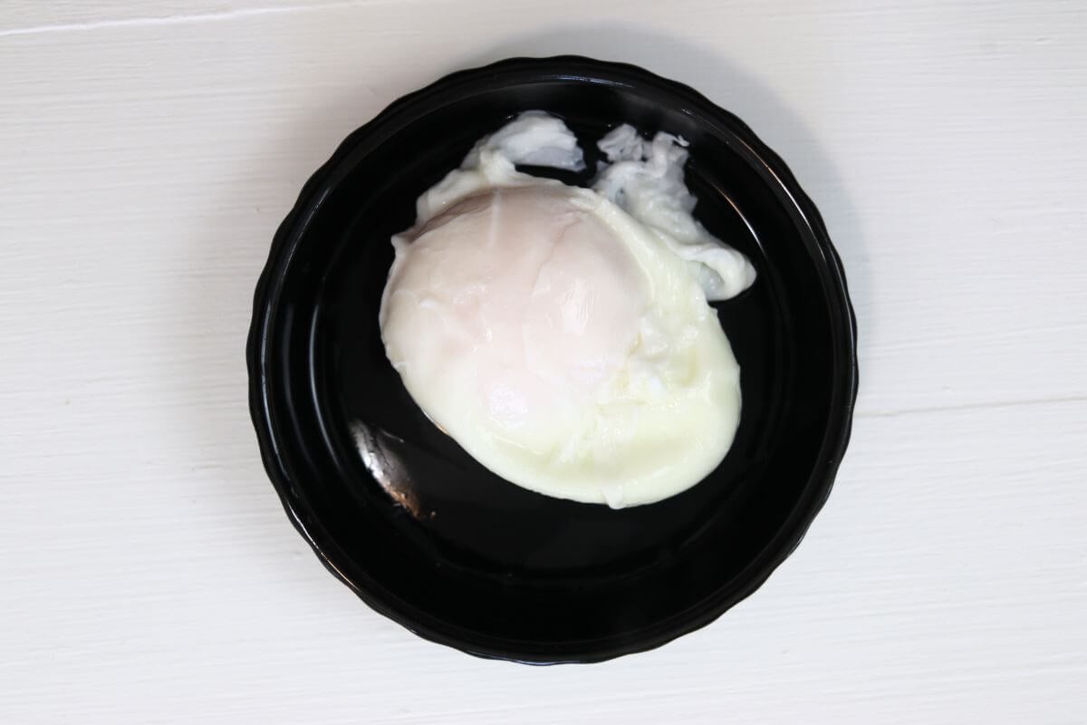 Poached egg on a black dish against a white surface.