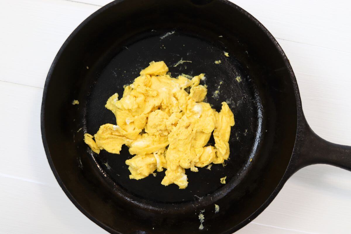 Scrambled egg in a cast iron skillet on a white surface.