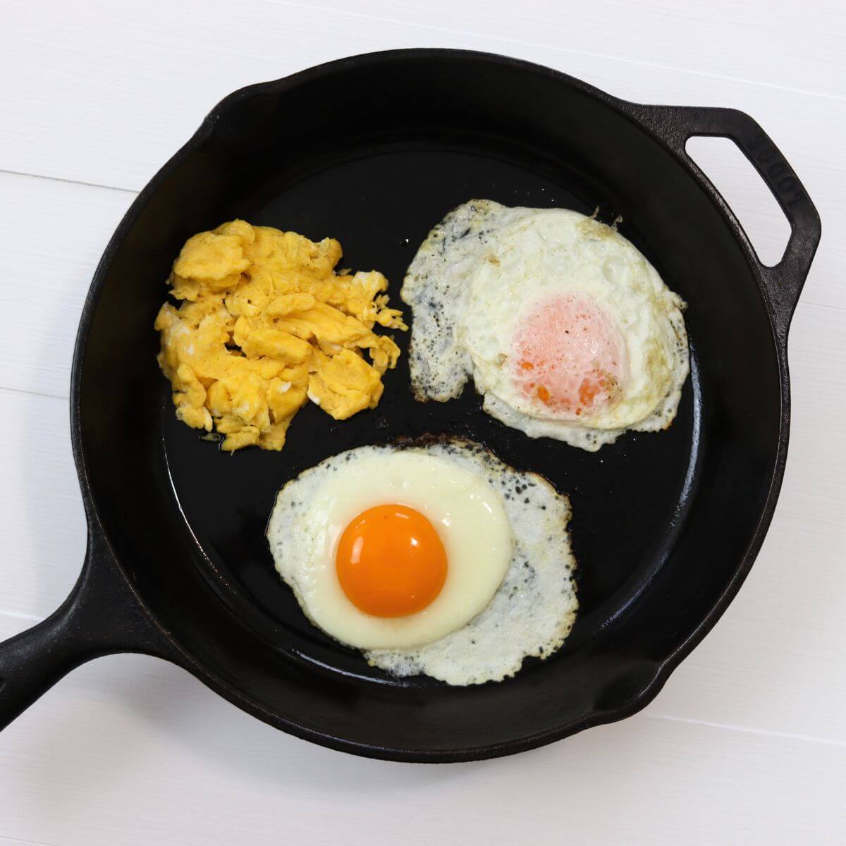 Cast iron skillet with scrambled eggs, basted egg, and sunny side up egg.