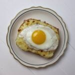 Croque madame with melted cheese and a sunny side up egg on top.