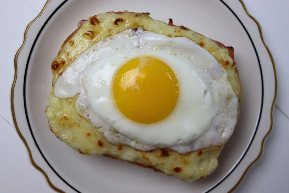 Croque madame sandwich topped with a sunny side up egg on a white plate.