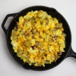Denver breakfast mess in a skillet with eggs, potatoes, ham, and melted cheddar cheese.