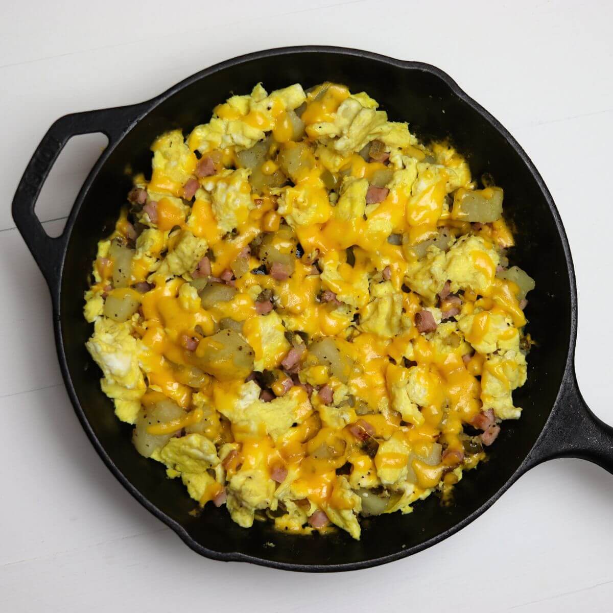 Denver breakfast mess in a skillet with eggs, potatoes, ham, and melted cheddar cheese.