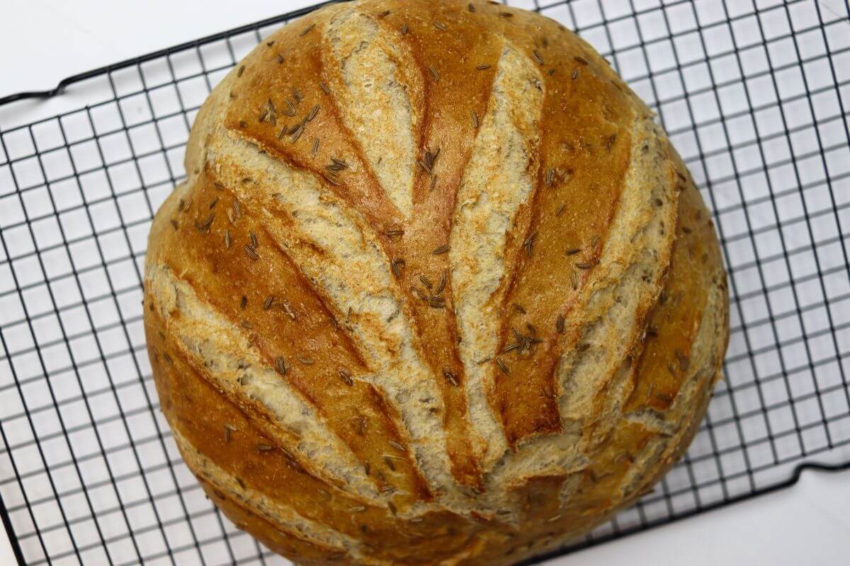 Rye bread loaf topped with caraway seeds on a wire rack.