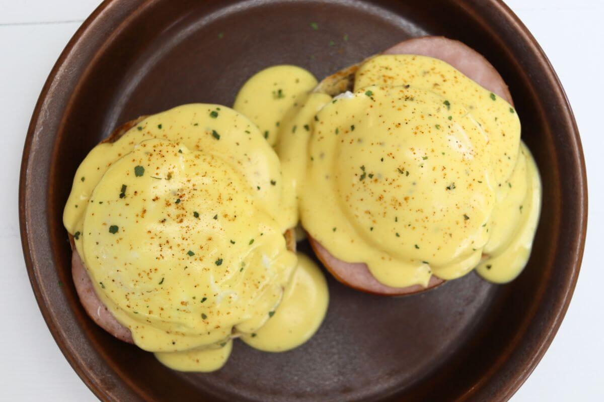 Eggs Benedict with Canadian bacon, poached eggs, and hollandaise sauce on a brown plate.
