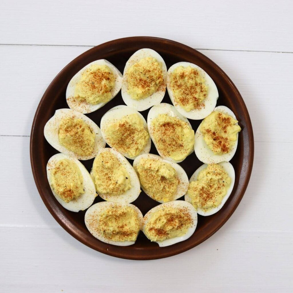Halved deviled eggs arranged on a round brown plate on a white surface.
