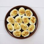 Halved deviled eggs arranged on a round brown plate on a white surface.