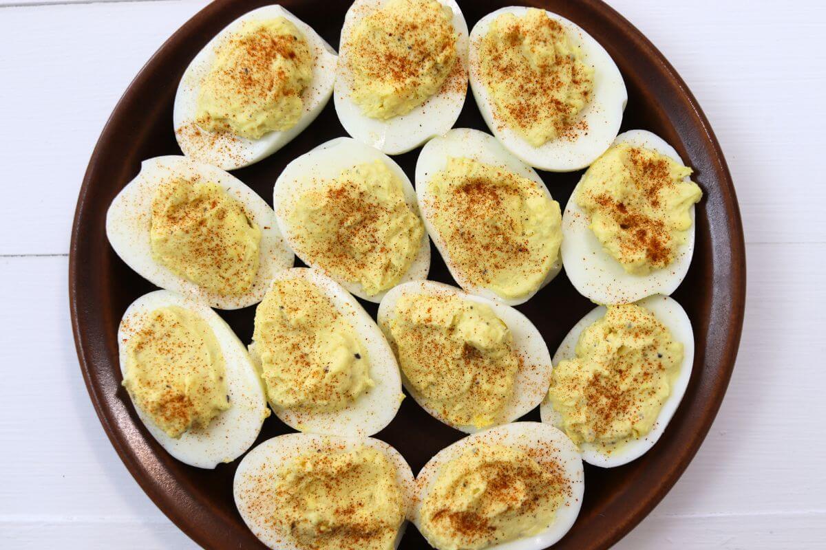 Farmhouse style deviled eggs on a brown plate with smoked paprika topping.