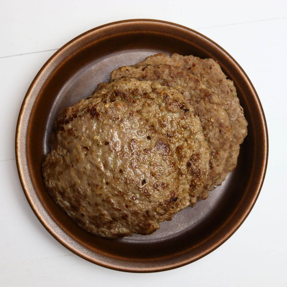 Fennel sausage patties stacked in a brown bowl on a white surface.