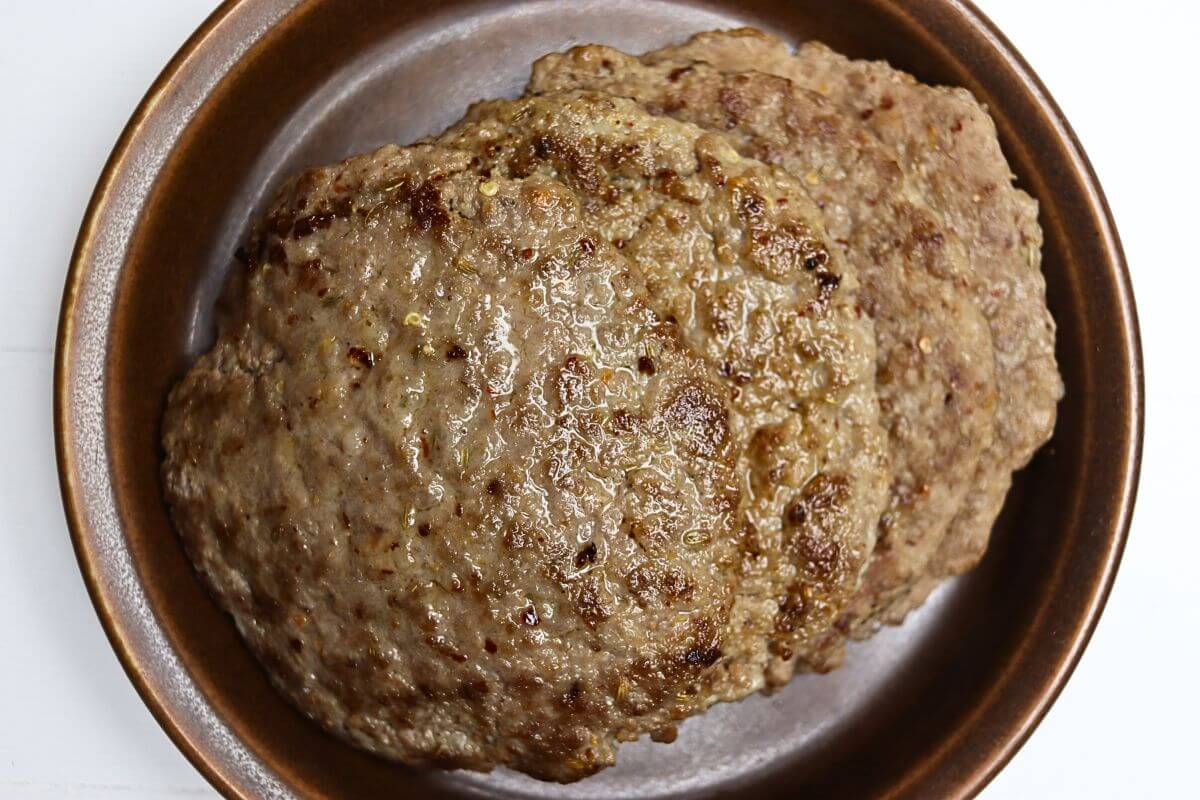Cooked fennel sausage patties with visible fennel seed in a ceramic bowl.