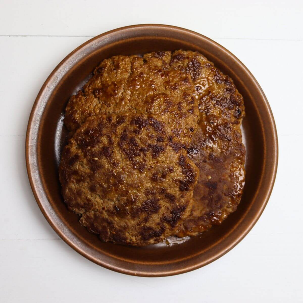 Homemade hot Italian sausage patties stacked in a brown bowl.