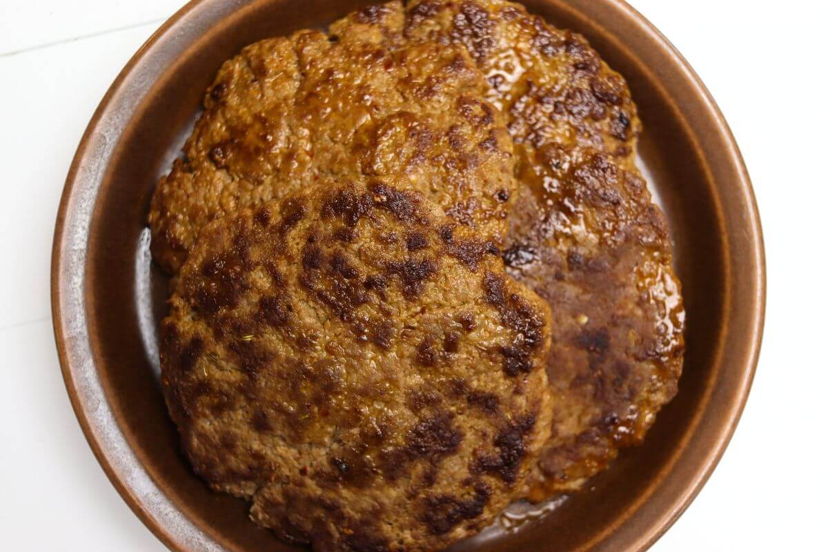 Cooked homemade hot Italian sausage patties in a round brown dish.