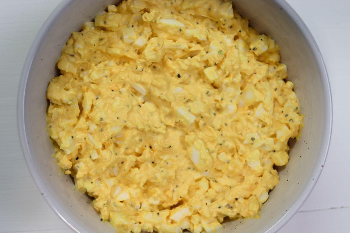 Homemade egg salad mixture in a white bowl on a light surface.
