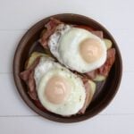 Open-faced ham breakfast sandwich topped with basted eggs on a brown plate.