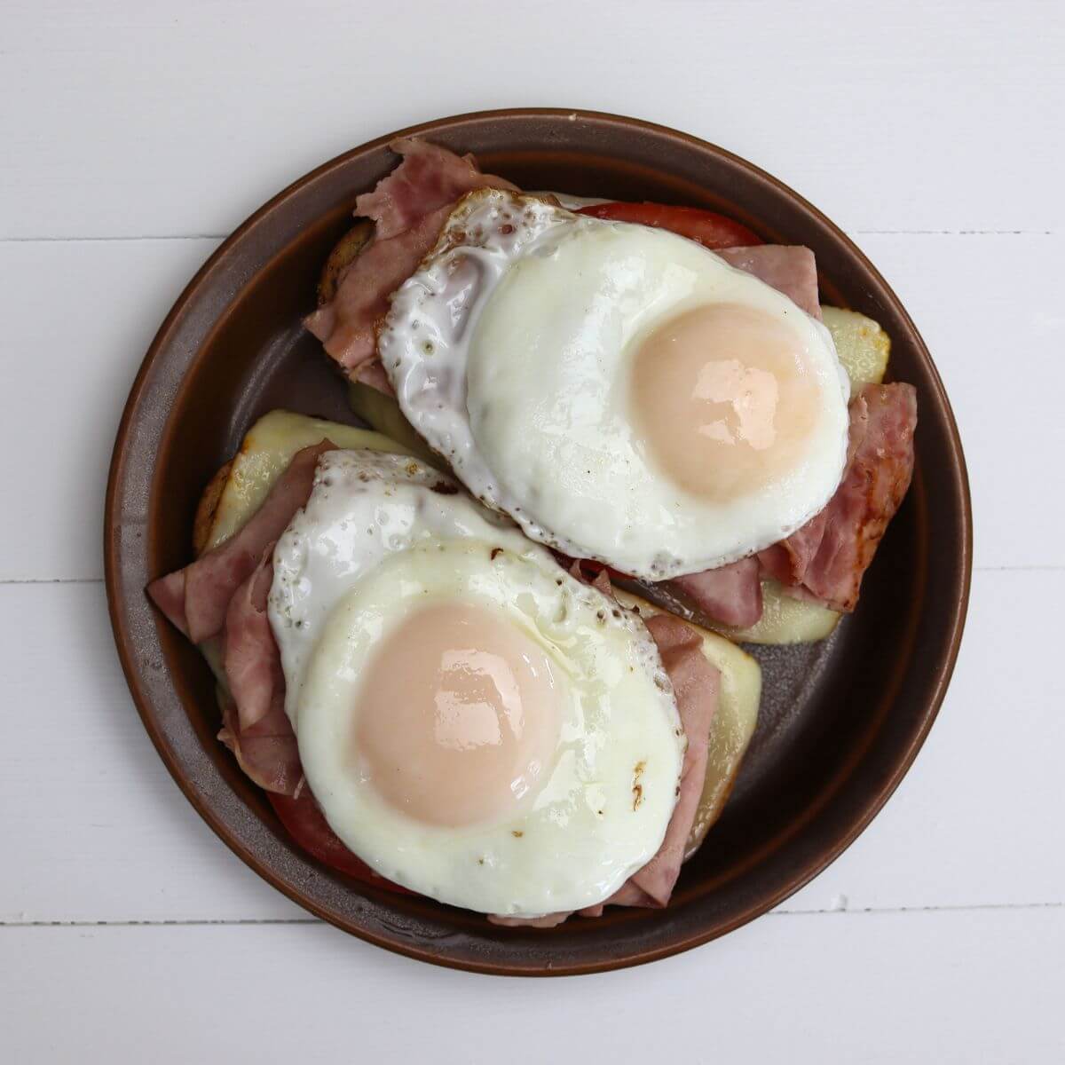 Open-faced ham breakfast sandwich topped with basted eggs on a brown plate.