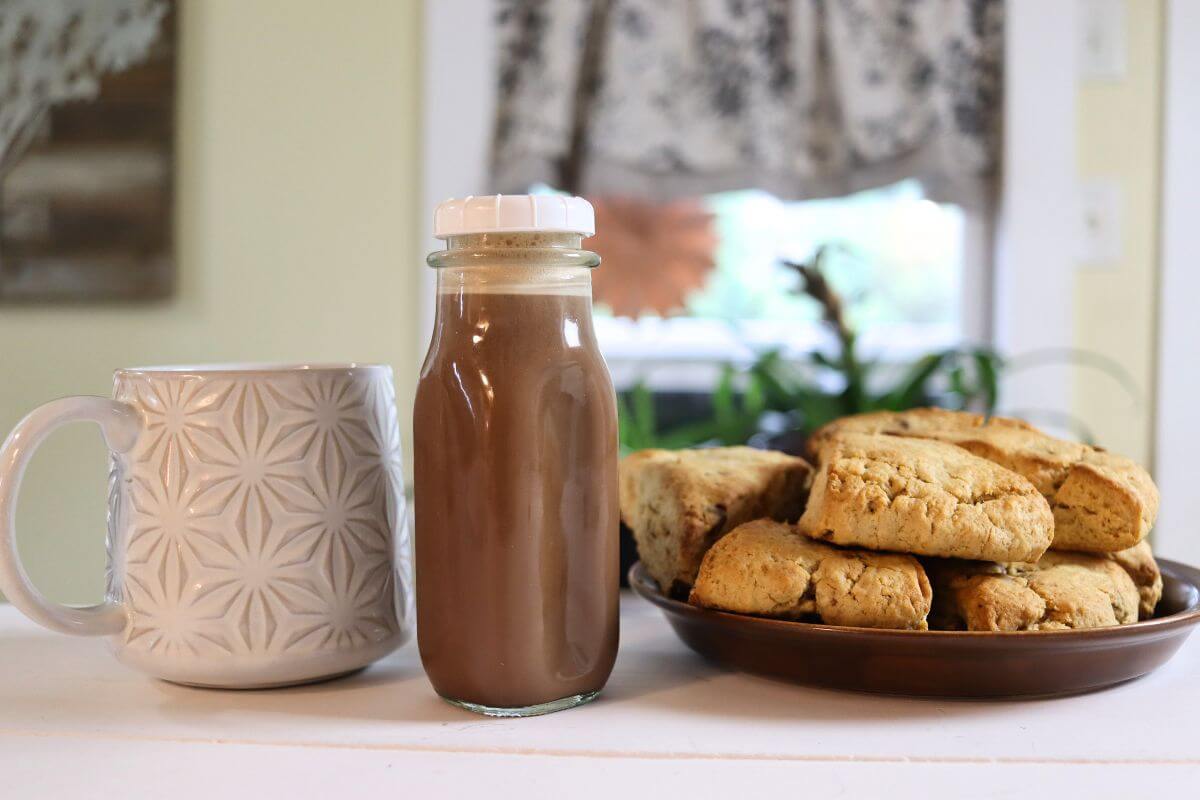 Bottle of peanut butter cup coffee creamer beside a mug and plate of biscuits.