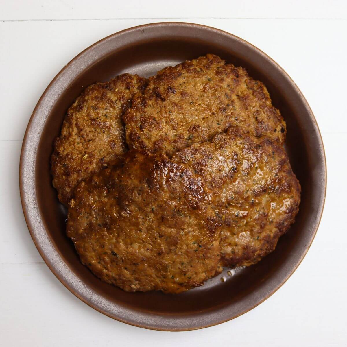 Sweet Italian sausage patties stacked in a brown bowl.