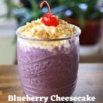 Purple milkshake in a glass jar with whipped cream and cherry. Text overlay reads "Blueberry Cheesecake Milkshake Recipe".