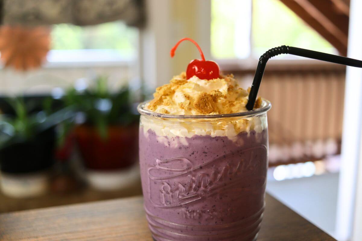 Purple milkshake in a glass jar topped with whipped cream, crumbs, and a cherry.