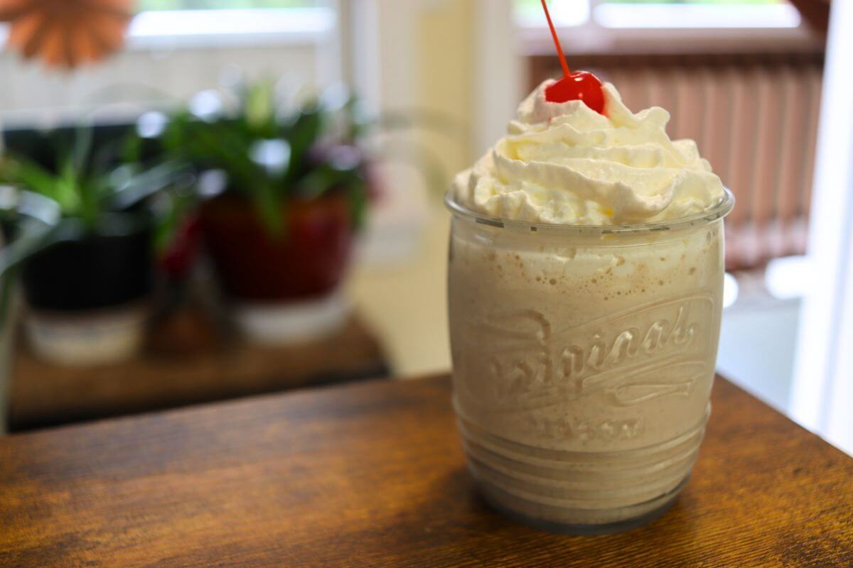 Chai milkshake topped with whipped cream and a maraschino cherry in a glass on a wooden table.
