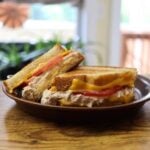 Two halves of a grilled tuna melt sandwich with tomato slices and melted cheese.