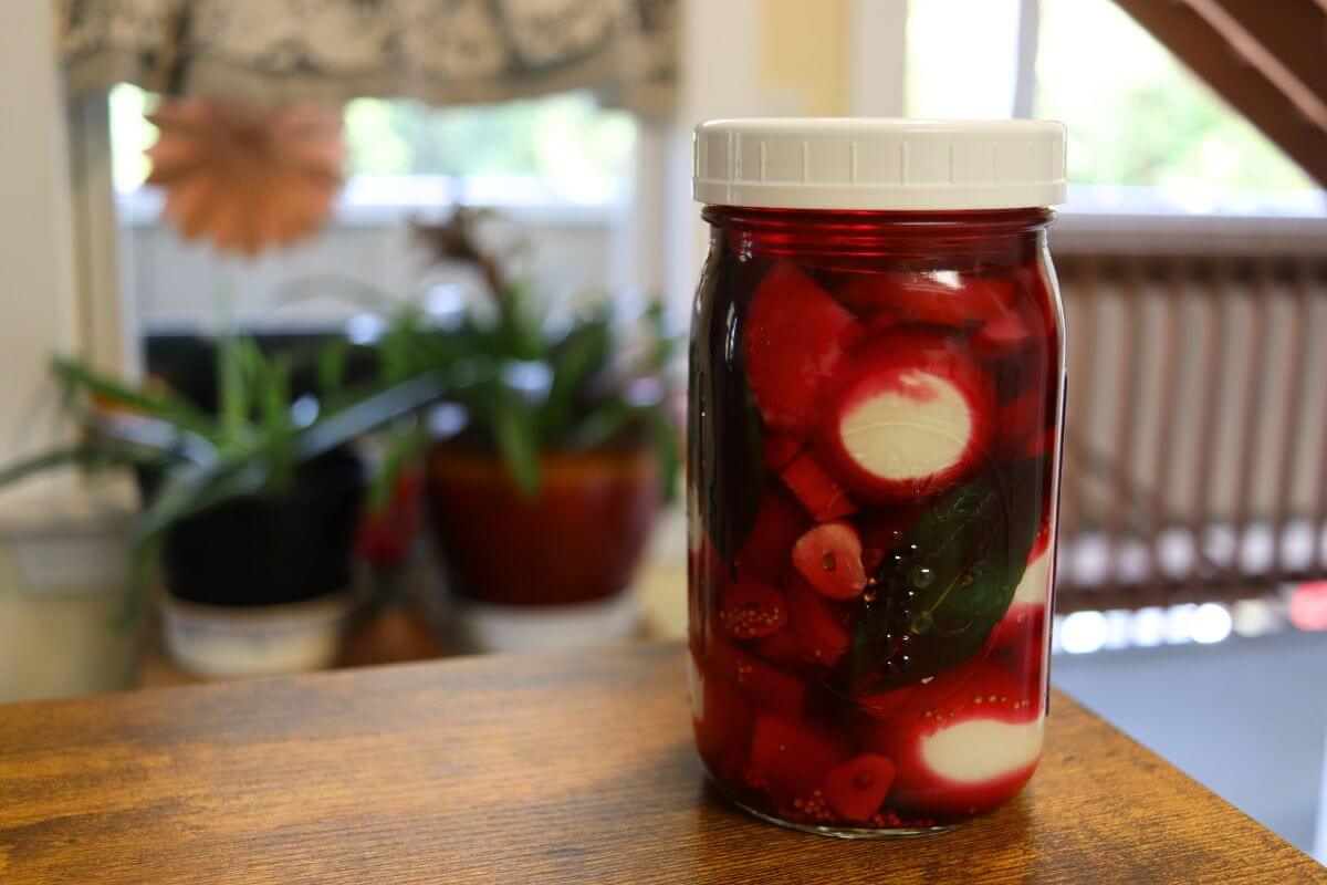 Farmhouse red beet pickled eggs in a mason jar with onions and bay leaves.