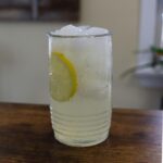 Glass of fresh squeezed lemonade with ice and a lemon slice on a wooden table.