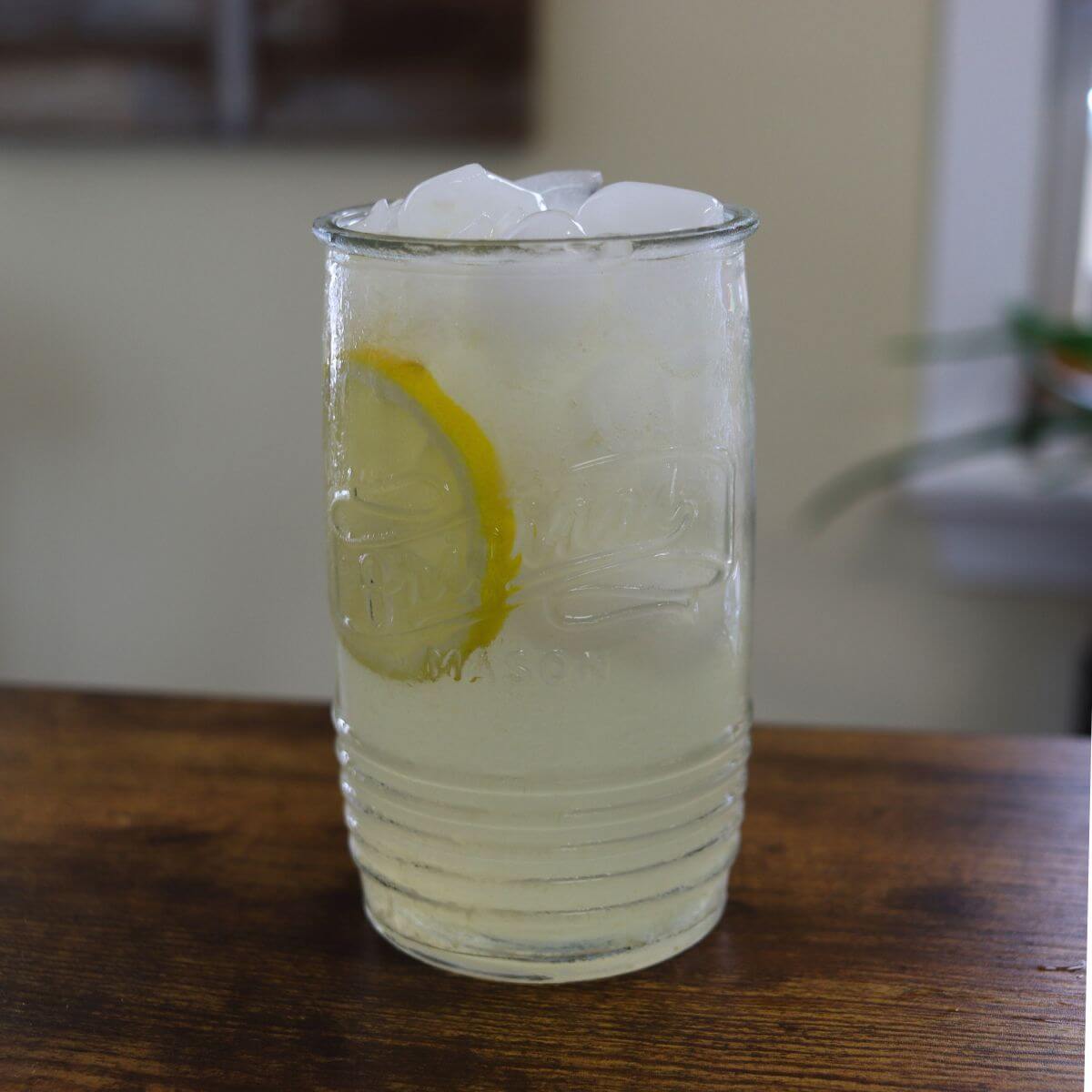Glass of fresh squeezed lemonade with ice and a lemon slice on a wooden table.