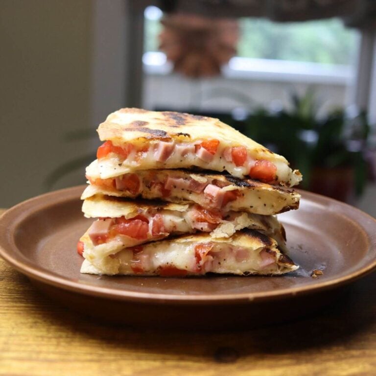 Stack of grilled ham and cheese quesadilla wedges filled with melted cheese, diced ham, and tomatoes.
