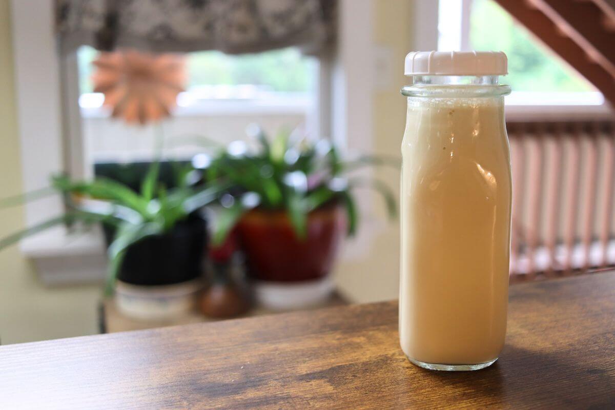 Glass bottle of homemade honey vanilla coffee creamer with a white lid on a wooden countertop.