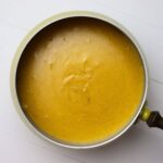 Fondue pot filled with nacho cheese fondue on a white surface.
