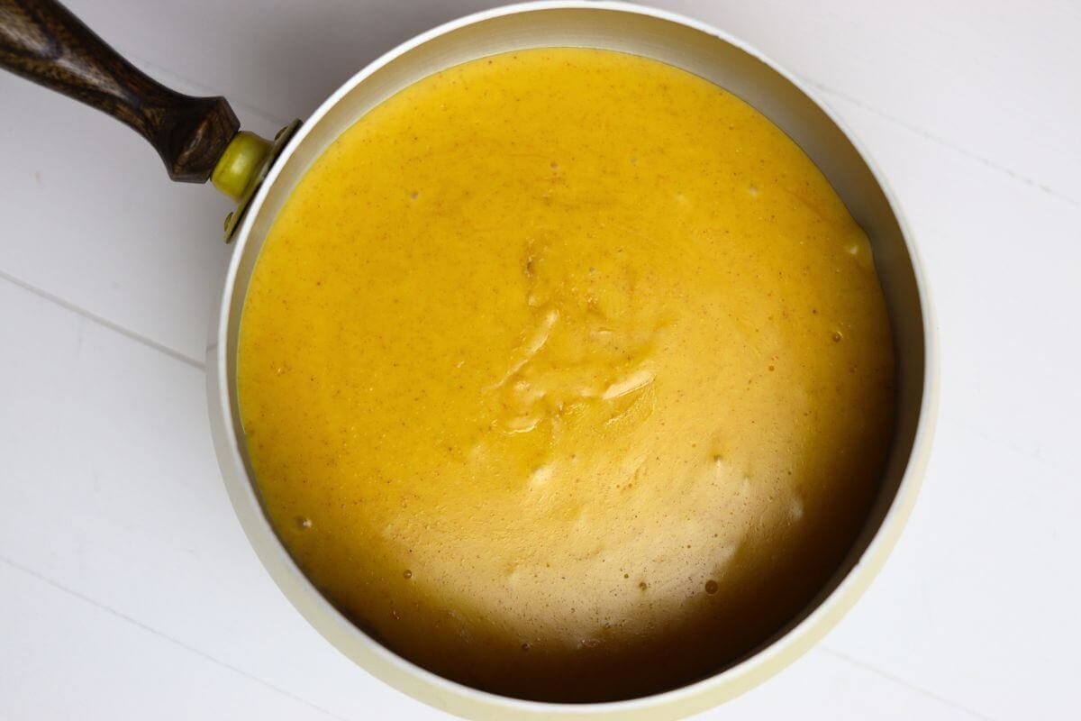 Nacho cheese fondue in a fondue pot with a wooden handle.