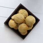 Bowl filled with round buttermilk biscuits on a white surface.