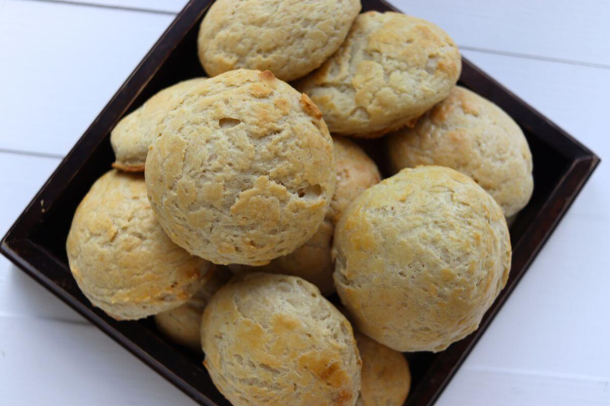 Several baked buttermilk biscuits stacked in a square serving bowl.